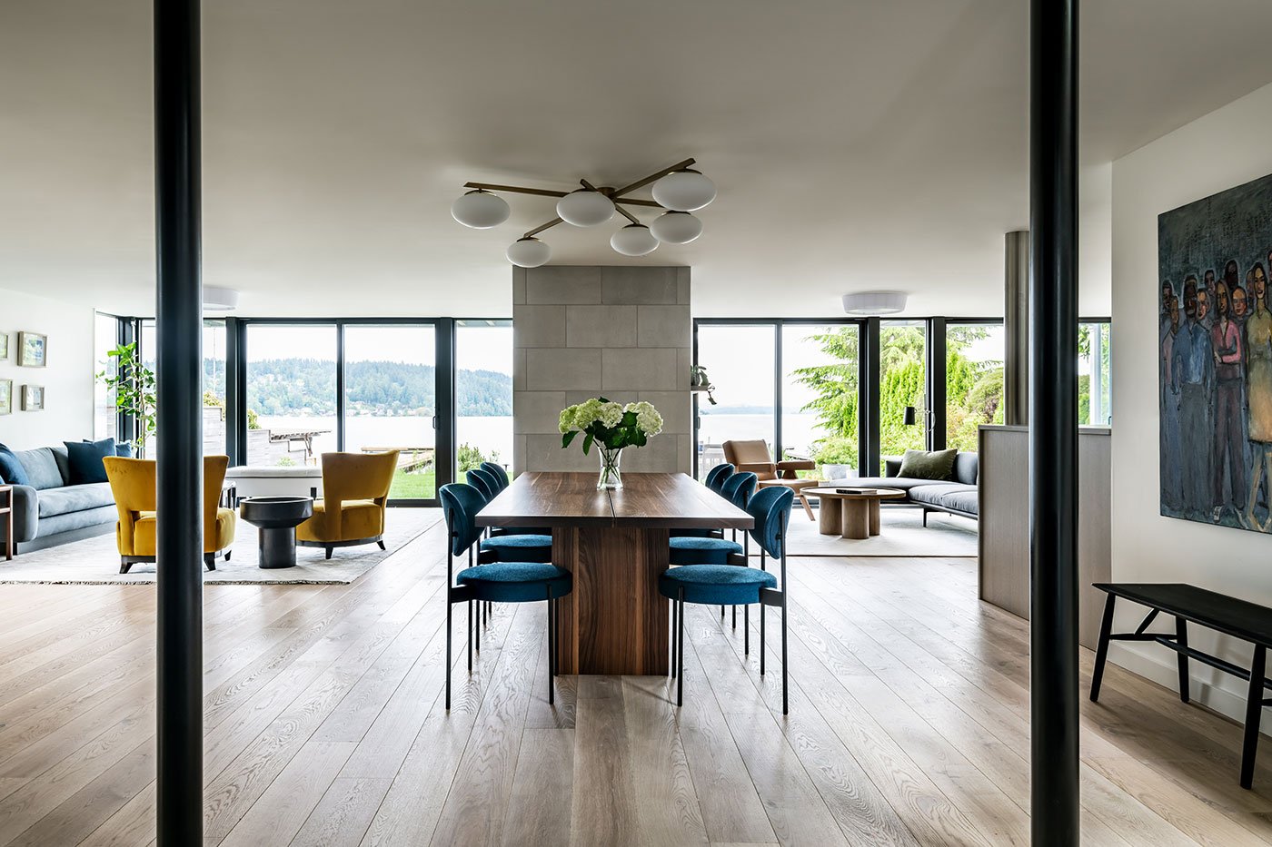 An open concept space with dining table and two living spaces facing a lakefront. 