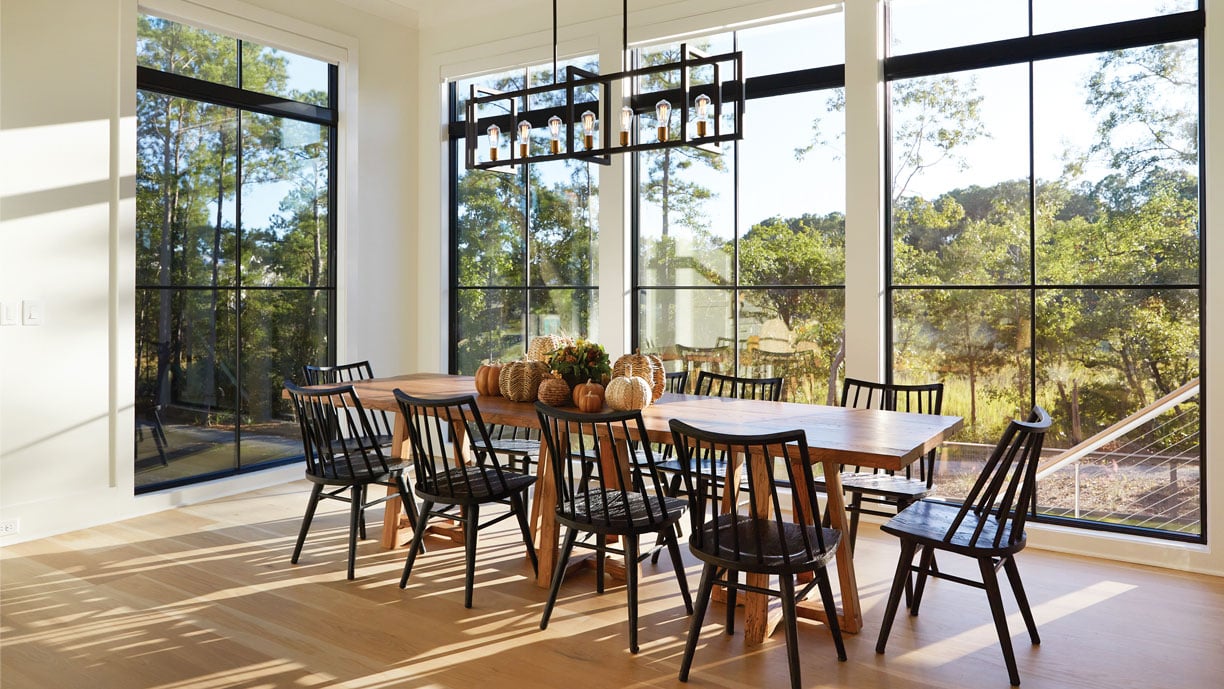 Dining room featuring Andersen Windows 400 Series Flexiframe picture and transom windows in black with traditional stops and 2x2 grilles.