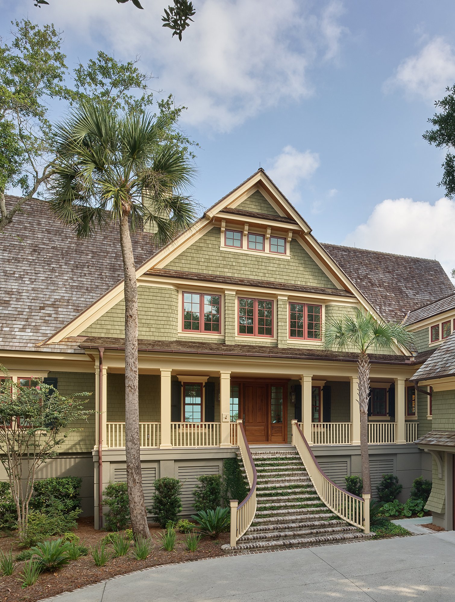 A multiple-story house with green shingle siding and steeply pitched gray shingle roof, with colonial grille patterns on the windows.