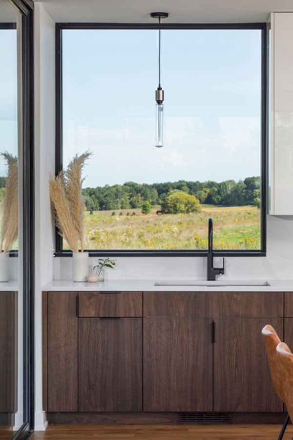 A kitchen sink with a picture window above it frames an expansive view of rolling prairie.