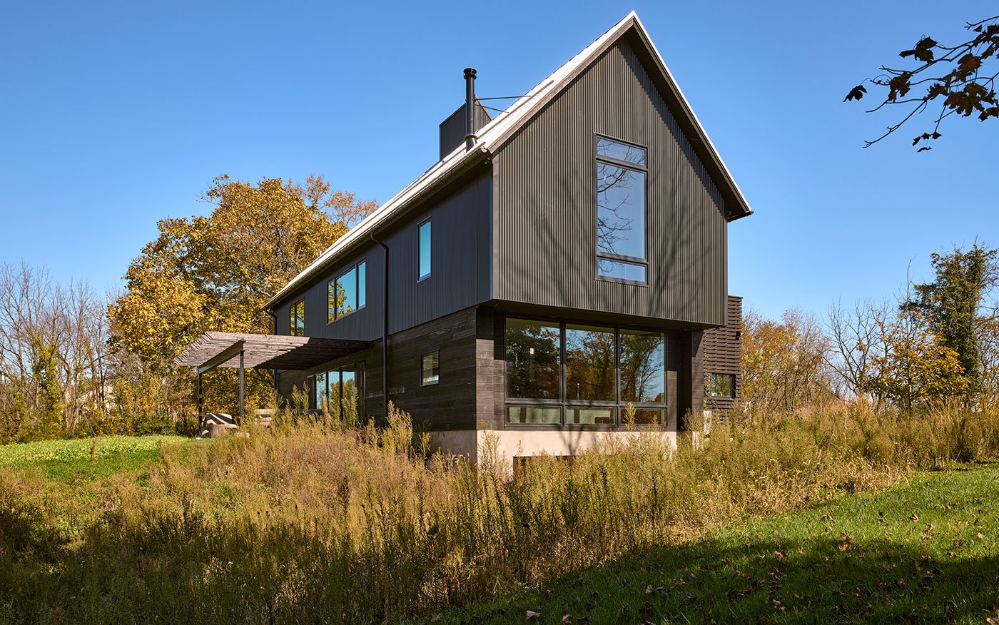 An exterior view of a barn-inspired home with black siding and large windows.