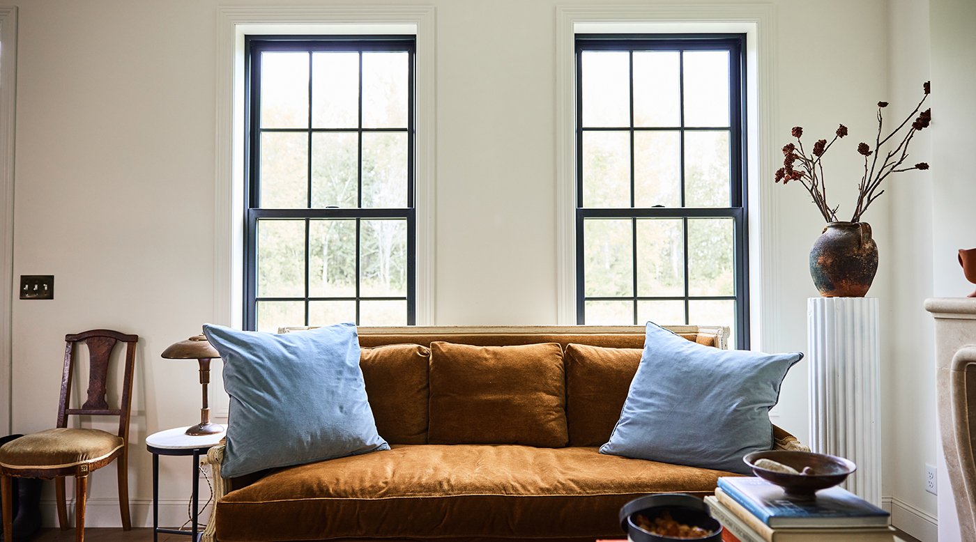 A bright and airy living room with black Andersen® 100 Series Double-Hung Windows featuring a colonial grille pattern.