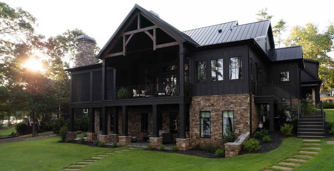the rear of a large, two-story, modern farmhouse nestled on a plush green lawn with two large stone pathways leading to the doors of the home.