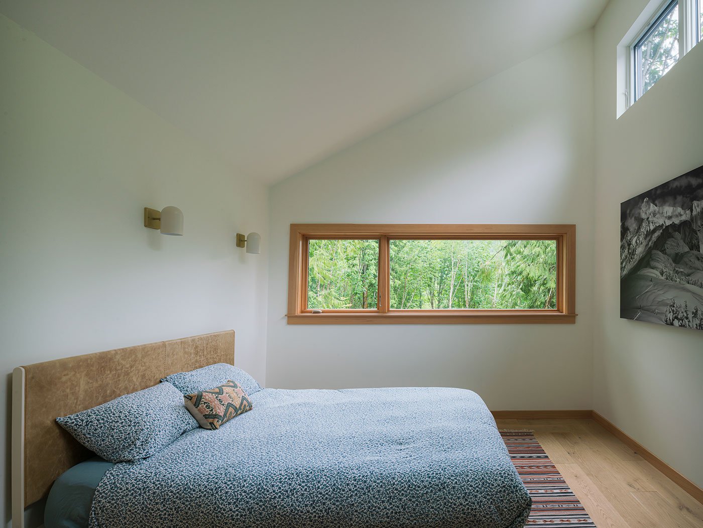 A bedroom with a sloped ceiling that has two rows of windows — one at ceiling height and one lower on the wall.