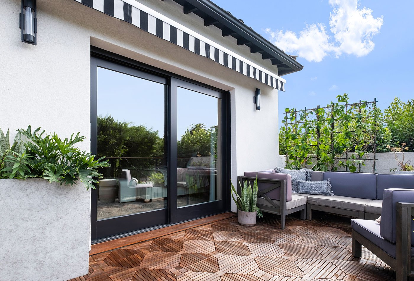 An exterior shot of a courtyard patio with outdoor furniture; a black, pocketing MultiGlide™ Door; and complimentary blue skies and surrounding greenery.