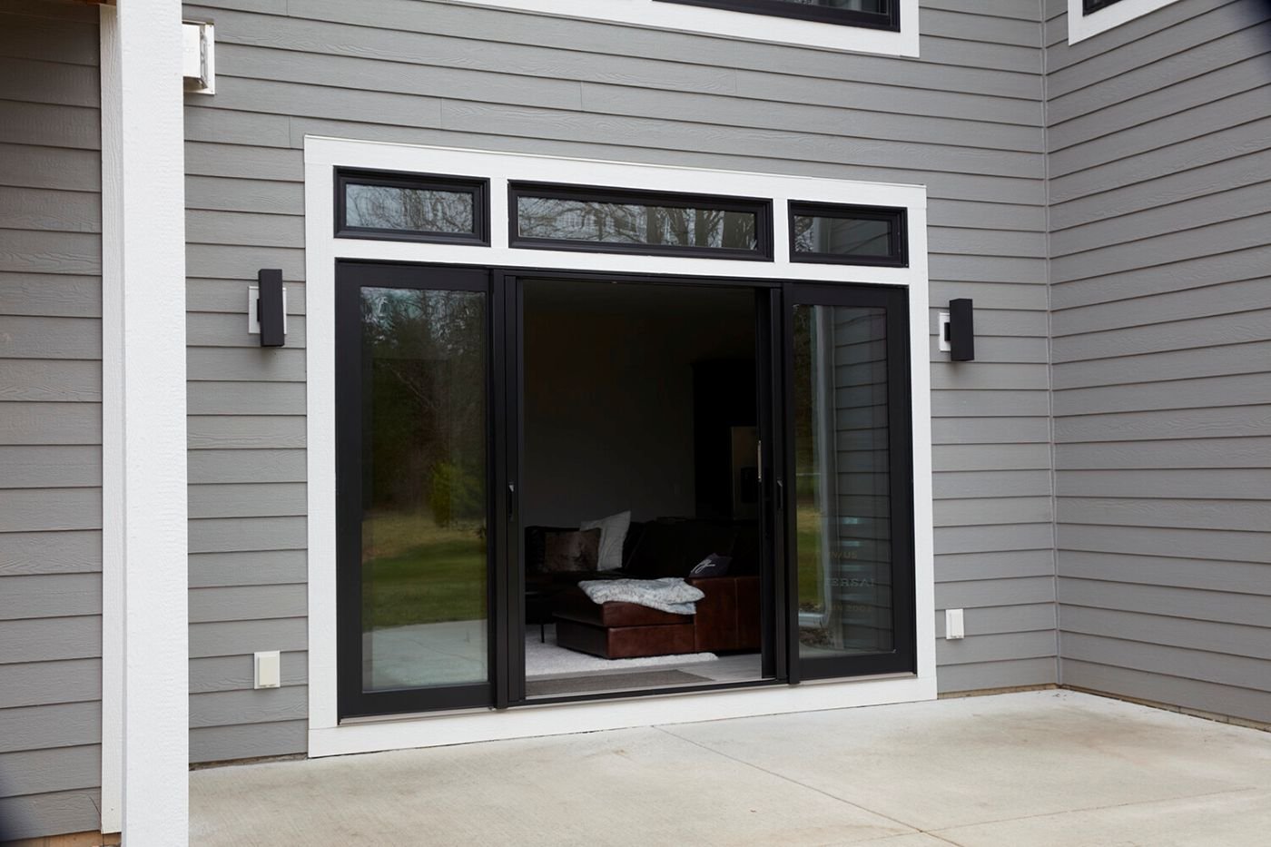 An open four panel gliding patio door with black frames and transoms. 